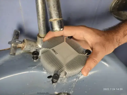an AMD stock cooler heatsink being washed under tap water.