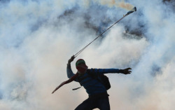 massconflict:  A masked Palestinian youth wearing a Hamas headband uses a sling-shot to throw back a tear gas canister towards Israeli forces during clashes outside the Israeli-run Ofer military prison, near the West Bank city of Ramallah.Nov19 2014Abbas