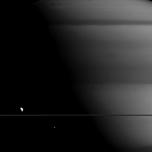 Two Of Saturn’s Moons Standing In Sharp Contrast Against Their Giant Companion