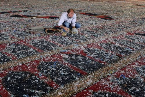 A man removes broken glass scattered on the carpet of a mosque heavily damaged by the August 4th, 20
