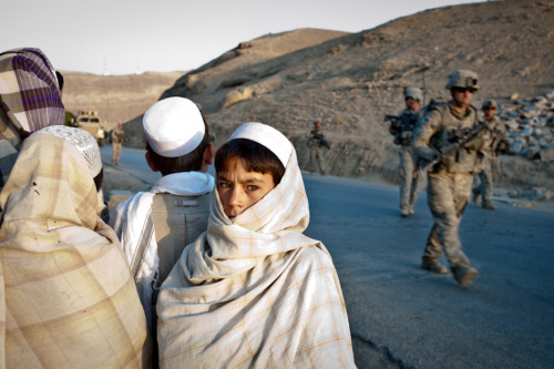 A cluster of young boys watches soldiers from Apache Company pass by on a morning patrol in the Tang