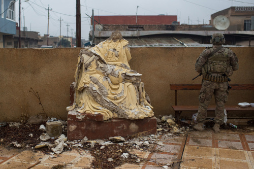 An U.S. Army soldier stands guard next to a defaced statue during Christmas Day mass at Mar Hanna ch