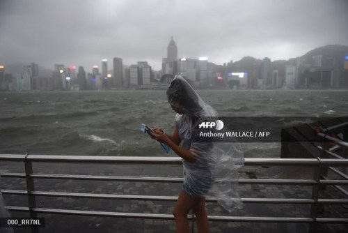 A woman uses her phone while wearing a plastic poncho along Victoria Harbour during heavy winds and 