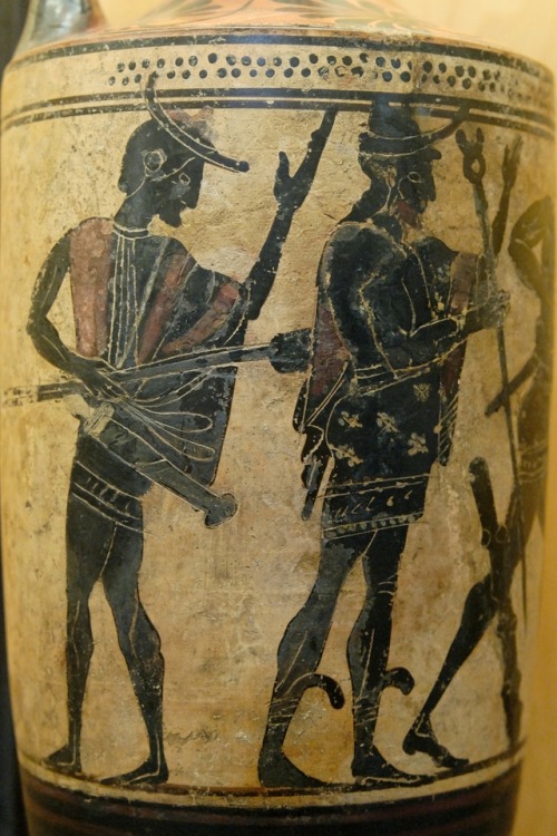 Heracles’ charioteer Iolaus holds his arrows, while the god Hermes watches Heracles grapple with the