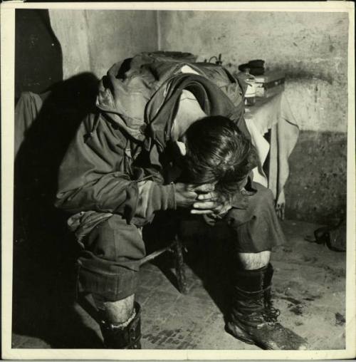 An exhausted US infantryman sitsin an aid station in Italy, hunched over and sleeping.  He has beeno
