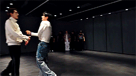 A gif from the dance practice. Ten is wearing a white crop top and Hendery is wearing a white zip up windbreaker.