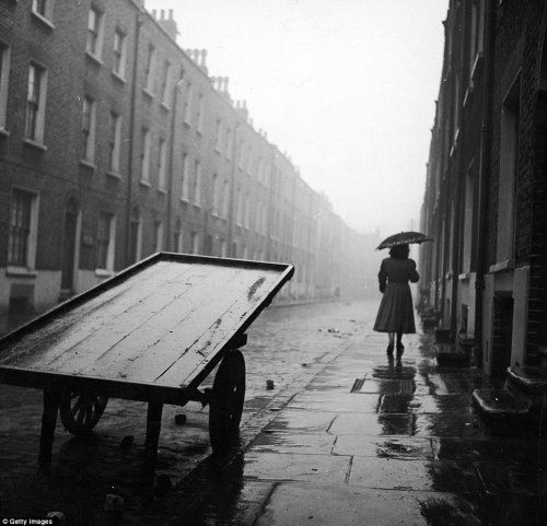 Getty Images. A woman walks down a rainy street in post-war Whitechapel. London. 1950s