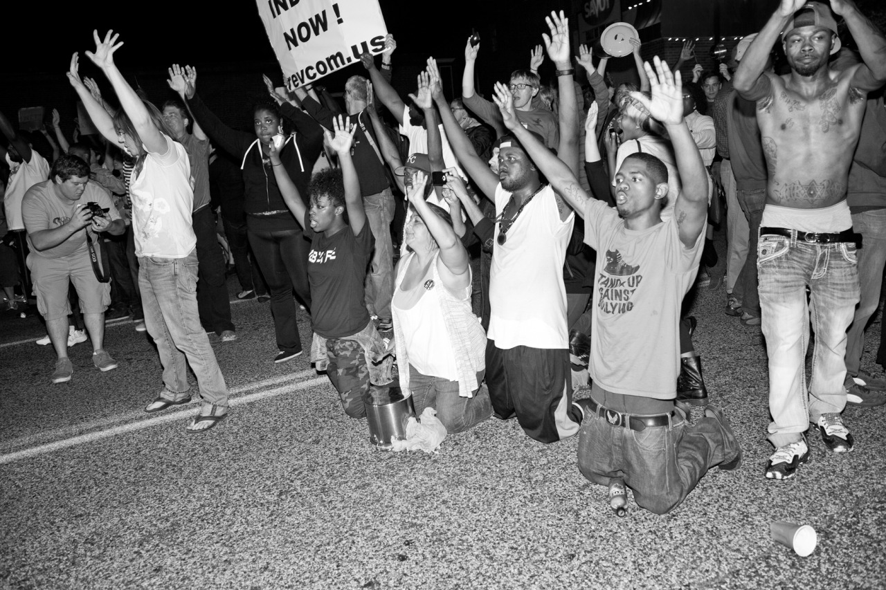Protesters kneel in the street with their hands raised as they are approached by oncoming police vehicles outside the Ferguson Police Department.
www.AmplifyFerguson.com
Ferguson Police Department ✚ September, 2014