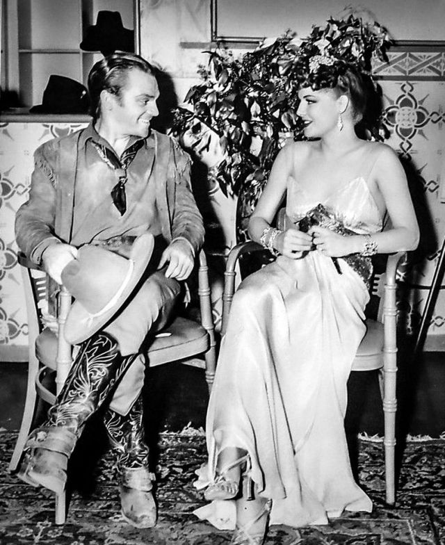 James Cagney (in his costume from 𝑻𝒉𝒆 𝑶𝒌𝒍𝒂𝒉𝒐𝒎𝒂 𝑲𝒊𝒅) visiting Ann Sheridan on the set of 𝑵𝒂𝒖𝒈𝒉𝒕𝒚 𝒃𝒖𝒕 𝑵𝒊𝒄𝒆 (1939). Photo by 