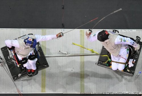 [ID: an overhead shot of a wheelchair foil fencer attacking his opponent.]Fencing at Montreal 2018!