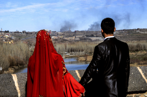 biladal-sham: A couple held hands for a wedding photo as smoke rose over Amed, Kurdistan, after clas