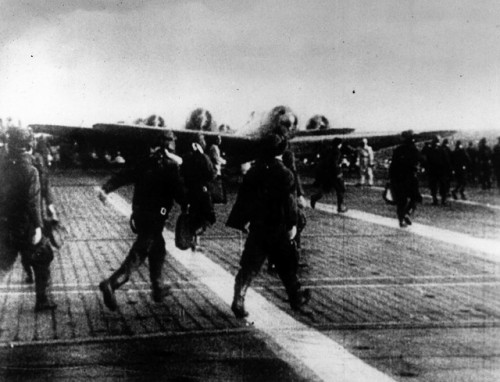 Japanese pilots heading for their aircraft, and dive-bombers spinningup on the deck of a carrier bef