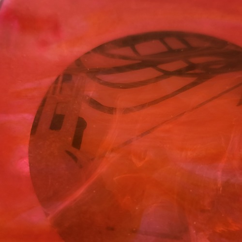 A close-up view of a section of the craft. A corner of rooftop and parts of the ribbon silhouette can be seen at the edge of the circle cut out. The detail shows the irregular distribution of color in the new resin layer. Orange, pink, and red colors blend and swirl together without distinct edges.