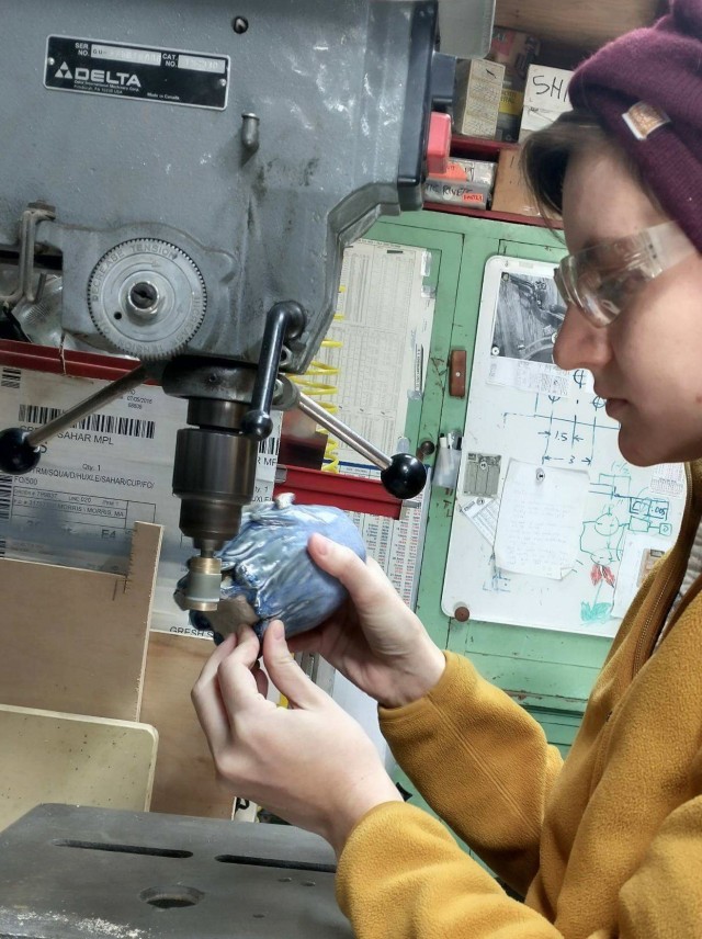 A person holding a small sculpture to the business end of a drill press.