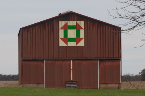 Bibb - 2511 Airport Rd Murray KY 8x8 Churn Dash
This simple quilt block in warm colors of rust, green and yellow hangs atop the Bibb family Tobacco Barn, Bobbi’s grandmother taught her how to hand quilt when she was a young girl. There were always...