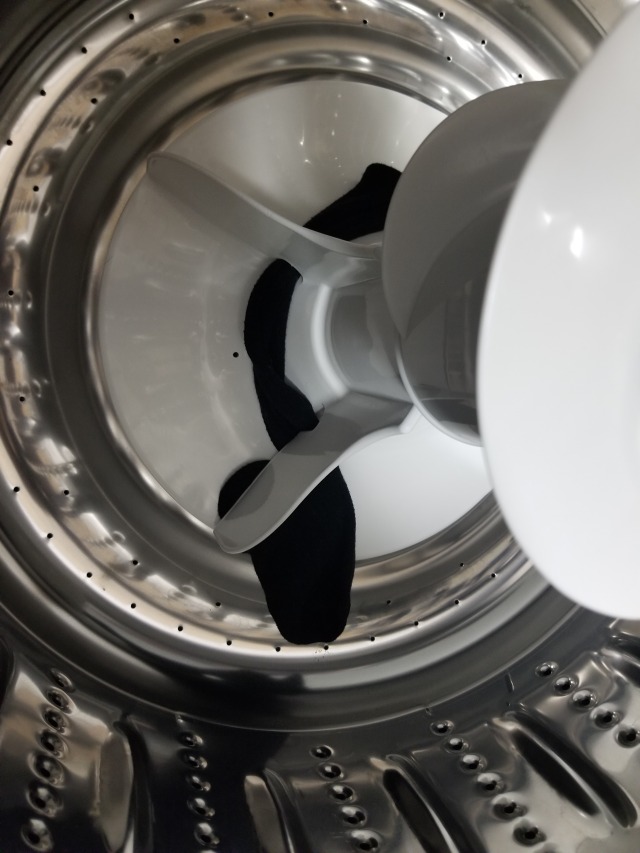 The inside of a washing machine drum. A black sock is caught underneath 3 of the blades, leaving it very entangled in the machinery. 