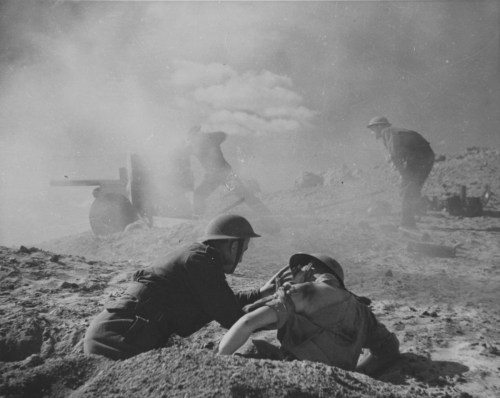 worldwar-two:A British soldier aids a comrade while a fellow soldier mans a 6 pounder anti-tank gun 