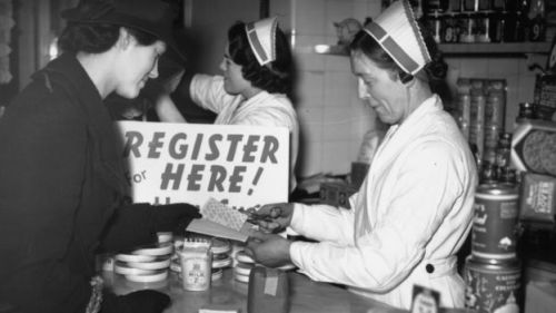 A woman shopping in wartime London has coupons removed from her ration book after buying her groceri