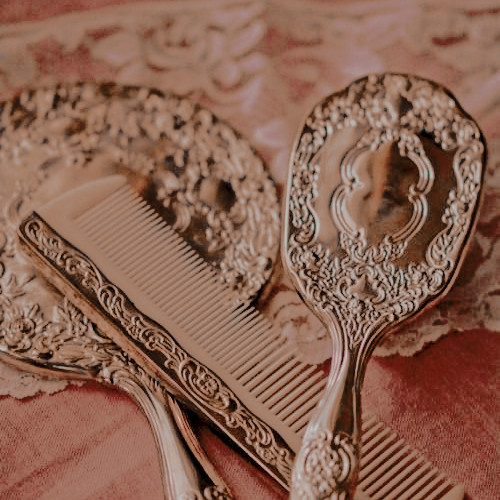 two elaborately carved gold mirrors and a gold comb on a pale pink surface.