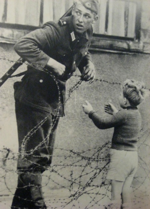 historicaltimes - An East German soldier helps a young boy cross...