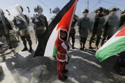 malcolmxing:    A Palestinian boy dressed as Santa Claus holds a Palestinian flag as he stands in front of Israeli soldiers during a protest against the controversial Israeli barrier in the West Bank village of al-Masara near Bethlehem December 20, 2013. 