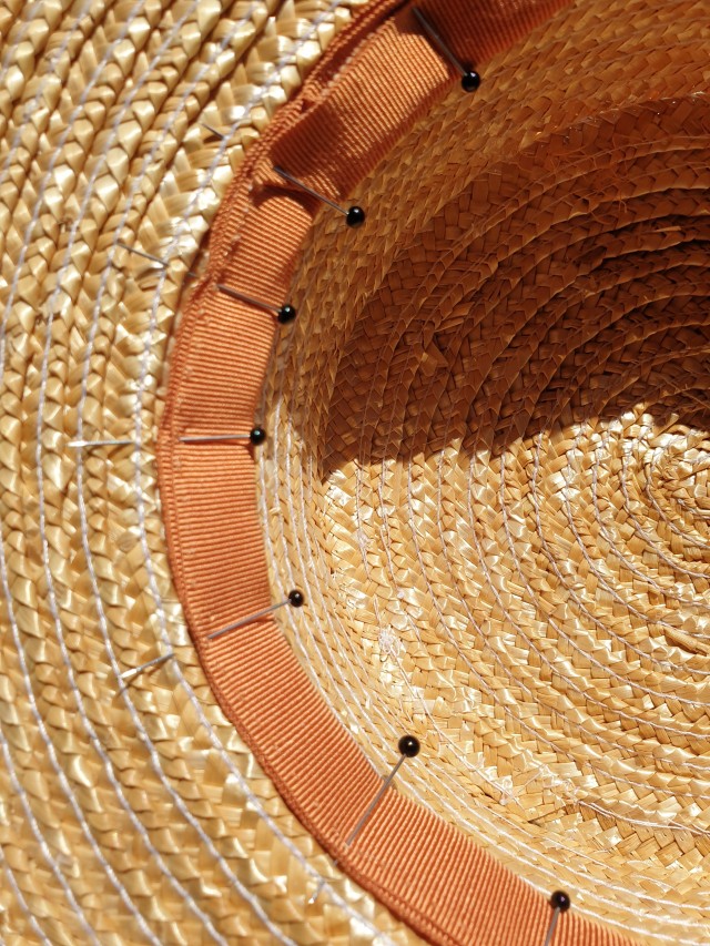 a closeup of an orange grosgrain ribbon pinned to the inside of a hat with black pins 
