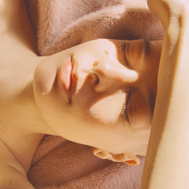 portrait of a person laying on a pink blanket in the sun with eyes closed