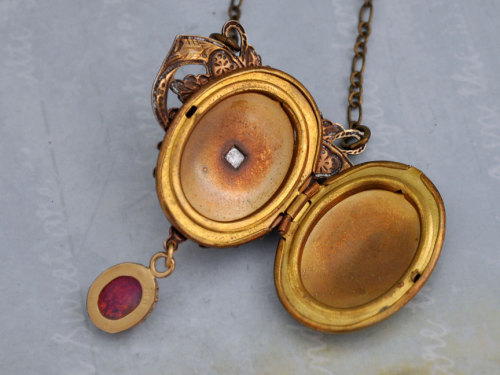 wickedclothes:  Victorian Pink Fire Opal Locket This brass locket features an ornate, Victorian style pattern. In the center of the locket rests a pink fire opal gem, and a pink fire opal also dangles from the bottom. Hung on an 18” chain. Sold on Etsy.