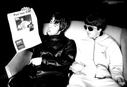 myterracottaheartbreaking: Liam Gallagher of Oasis, sticks his tongue out at a picture of Ian Brown [The Stone Roses] in the New Musical Express, while his brother Noel Gallagher looks on.  Newport, Gwent. Photo by  📷: Kevin Cummis. (May 03, 1994)