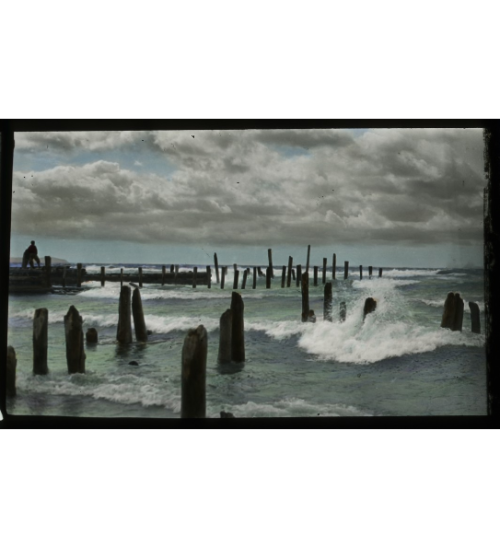 Hand tinted Lantern slide showing the image of waves on a lake and what appears to be dock posts in 