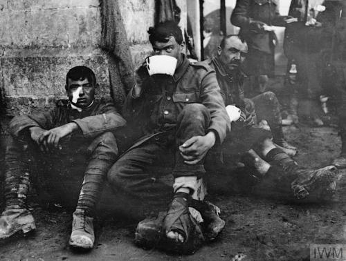 Three wounded British soldiers, one drinking from a bowl, in a dressing station in a churchyard at M