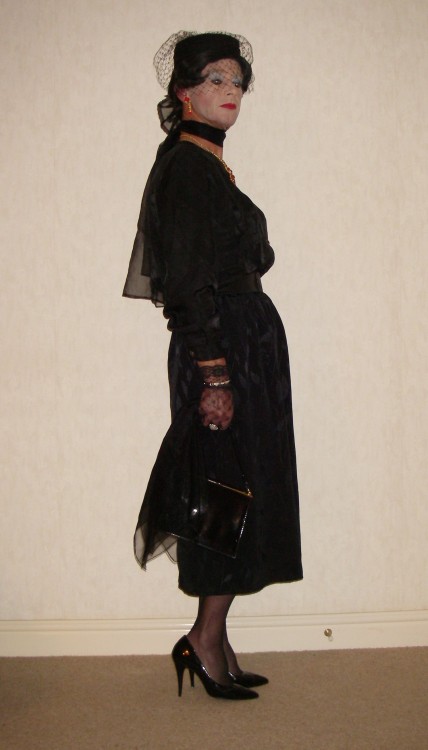 A black satin blouse with satin skirt. Wearing a veiled hat and with chiffon scarves and a handbag