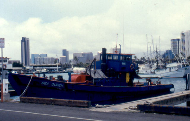 The wooden sampan Sea Queen is tied to a dock in a harbor with other small boats behind it.