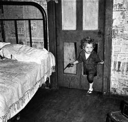 lettersfrombeachhead:mosertone:Coal  miner’s child using a hole in the door to enter a bedroom with a  smoking pipe in one hand and a gun in the other in Bertha Hill, West  Virginia. Photo by Marion Post Wolcott. 1938