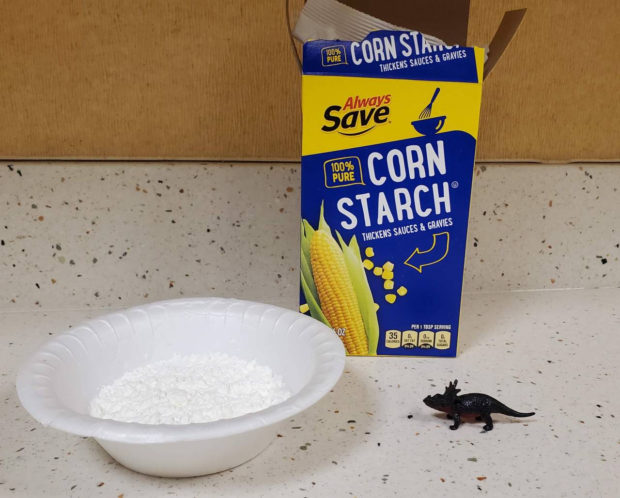 Box of cornstarch, styrofoam bowl, plastic dinosaur