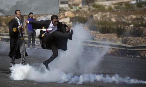 A lawyer in his official robes kicks a tear gas canister back toward Israeli soldiers during a demon