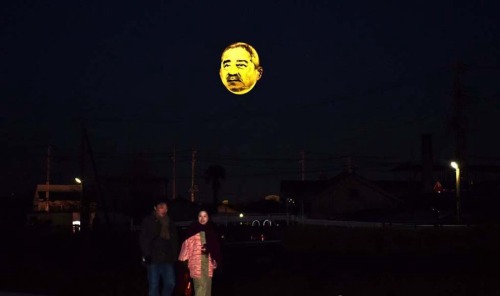 ofools:hollowedskin:shihlun:A giant helium balloon bearing the face of an ojisan (middle-aged man) a