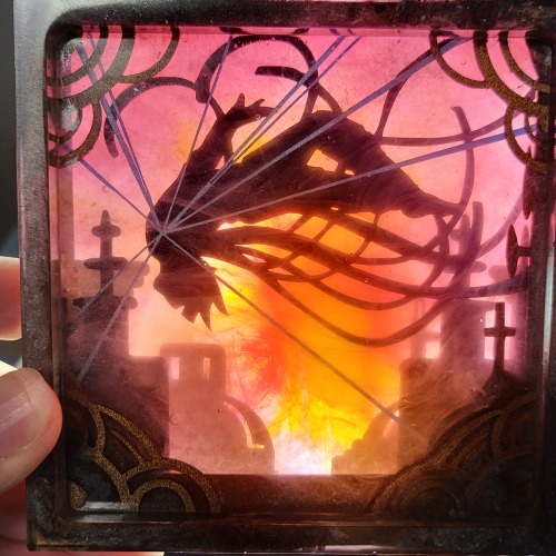 A bright light placed behind the resin lights everything up distinctly. The silhouette of the figure stands out starkly against the red sky. The swirls of red, orange, and pink ink in the final resin layer resembles fire in the sun cut-out. The gray buildings become slightly translucent, creating an illusion of fading into distant atmosphere. The swirls of white ink are nearly indiscernible