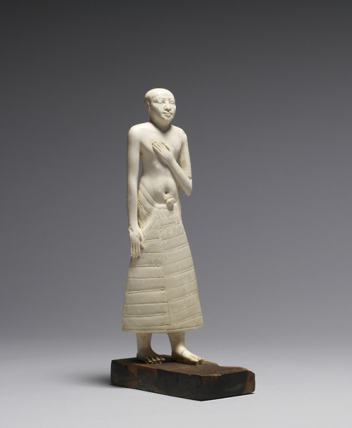 Ancient Egyptian ivory figure of a standing male dignitary, seen in three-quarters view.  Artis