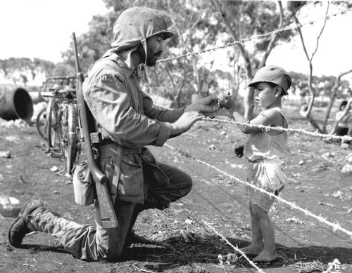 historylover1230: A US Marine gives candy to a Japanese child through the barbed wire fence of an in