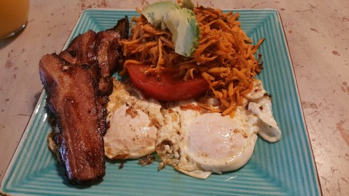 Breakfast of uncured bacon and eggs, fried tomato, shredded sweet potatoes and avocado