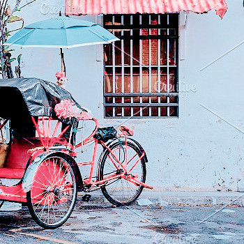 a pink cycle rickshaw with a blue umbrella is parked outside a barred window of a white-walled south asian house. 