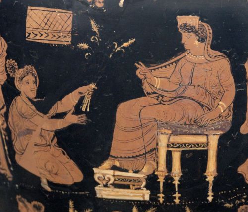 Demeter, enthroned and extending her hand in a benediction toward the kneeling Metaneira, who offers