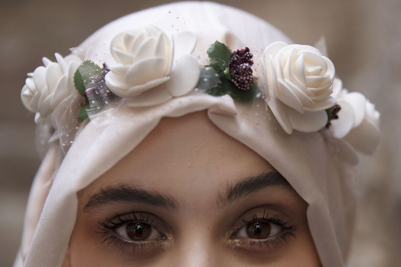 Una giovane donna palestinese indossa una corona di fiori sul suo hijab e accenti dorati nel trucco degli occhi nella Città Vecchia di Gerusalemme mentre si reca alla preghiera nel complesso della moschea di Al Aqsa che segna Moulid al-Nabi, il...