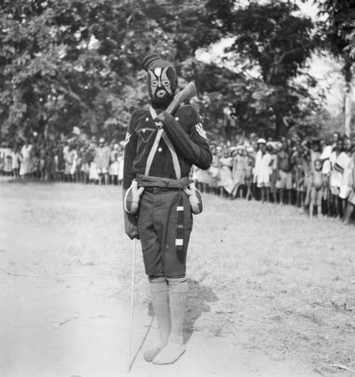 ukpuru:“[Igbo] Ghost police sargent standing with a replica wooden rifle in one hand and a stick in 