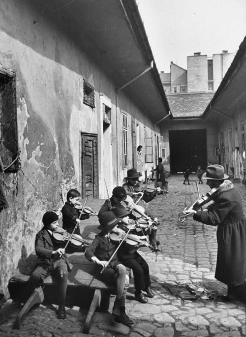 Roma children being taught to play the violin in a courtyard of one of the poorer houses of Budapest