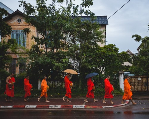 A line of Buddhist monks walk barefoot along a street in...
