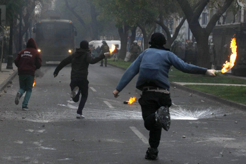 politics-war:  Protesters run holding Molotov cocktails to throw at police in violent clashes during a student demonstration in Santiago, Chile, on June 26, 2013. Teachers, dock workers and copper miners joined students in a nationwide demonstration to