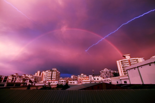 sixpenceee:    A rainbow appears in the sky as lightning strikes during a rainstorm on May 13, 2012 in Haikou, China. Photo credit: China Foto 