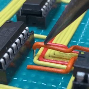 a set of n gifs of a person assembling a circuit board. they use tweezers to put the wires into the holes in the board next to the logic chips.each wire has been bent into shape to lie in perfect straight lines and neat corners, like piping in a house.